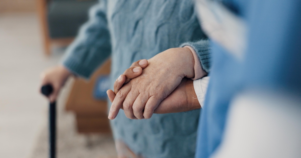 Image of elderly woman walking in a nursing home holding a person's hand