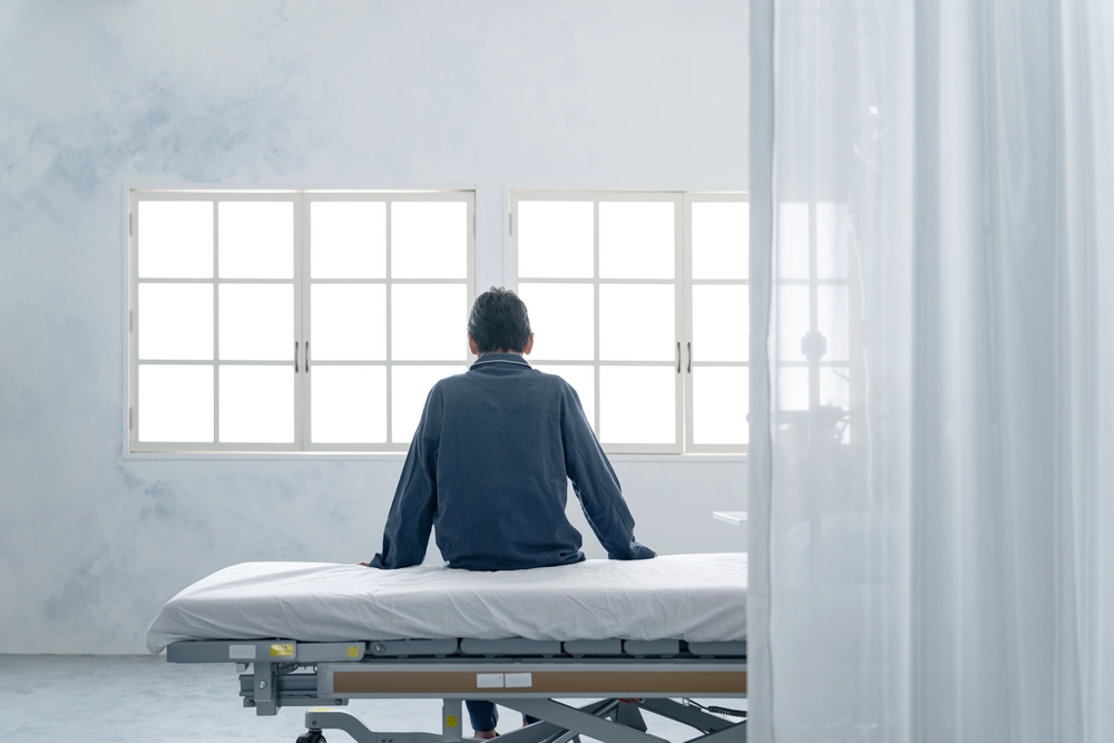 Patient sitting alone on a hospital bed near a window, symbolizing isolation and inadequate supervision in a mental health facility