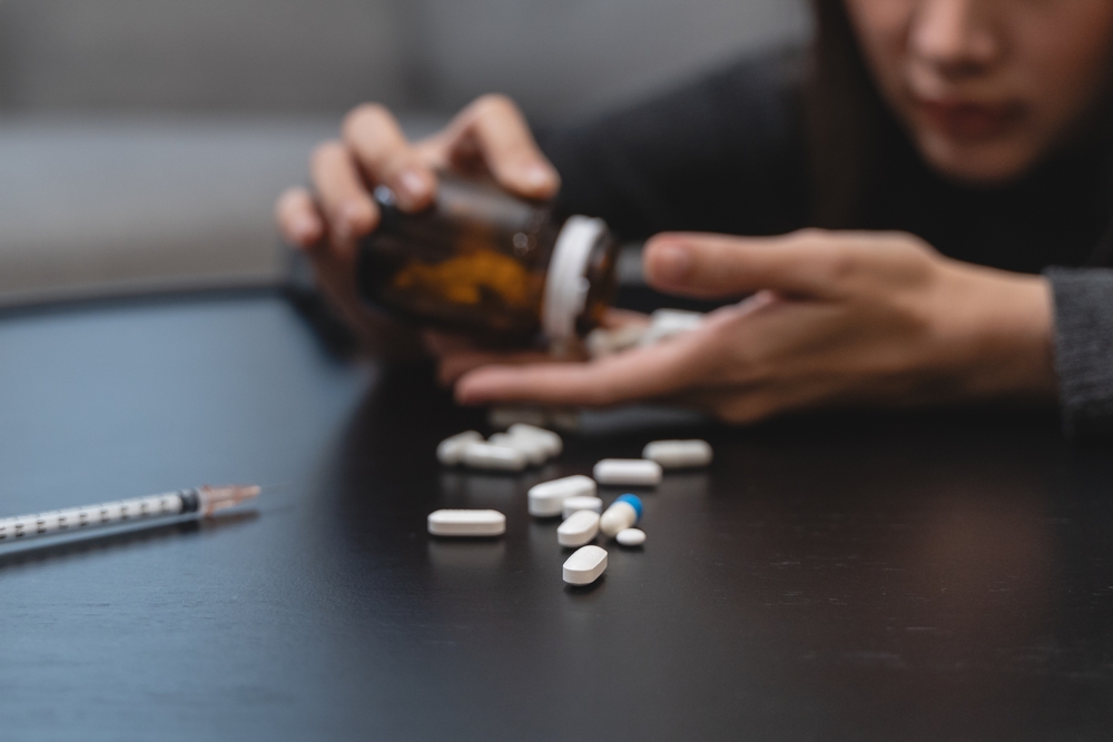 Person holding pills beside a syringe, symbolizing lack of supervision and overdose risk in a Florida rehab facility.
