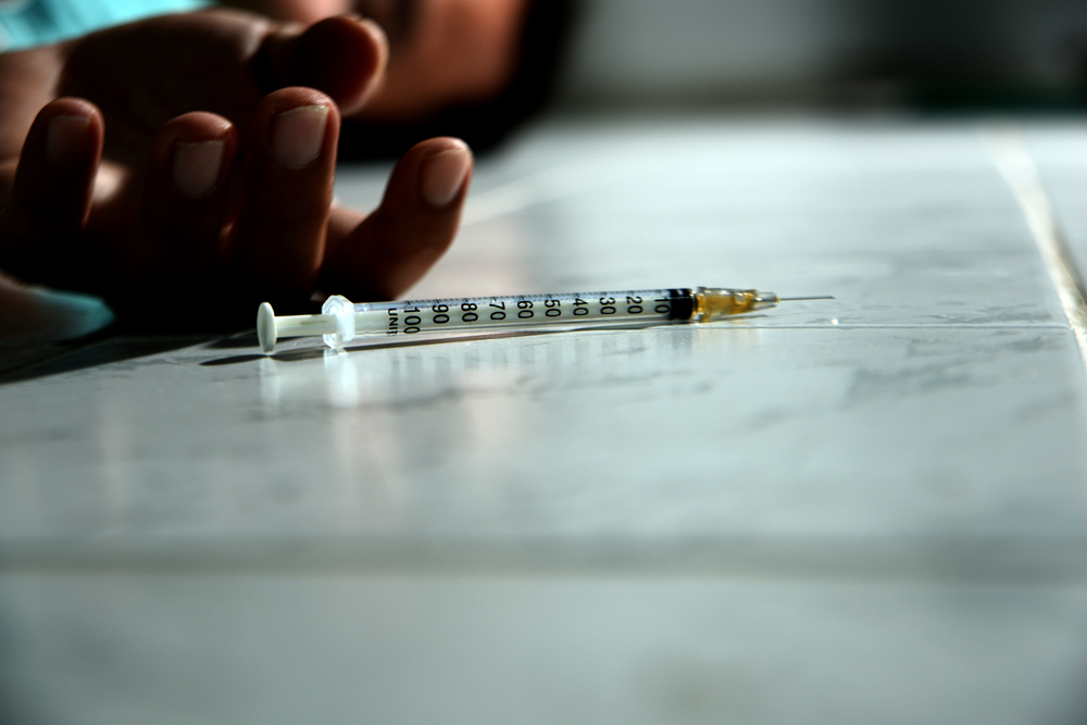 Close-up of a person’s hand on the floor beside a syringe, representing a fatal overdose in a Florida rehabilitation facility.