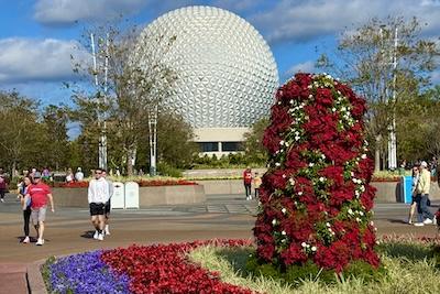 Picture of Epcot ball with flowers in the foreground and visitors walking by